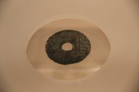 An ancient Chinese bronze coin with a square hole in the center displayed in a case