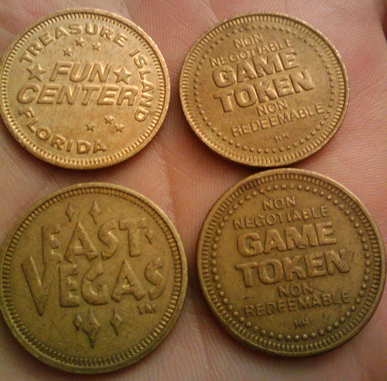 Four brass arcade tokens marked Game Token Non Negotiable Non Redeemable held in a hand