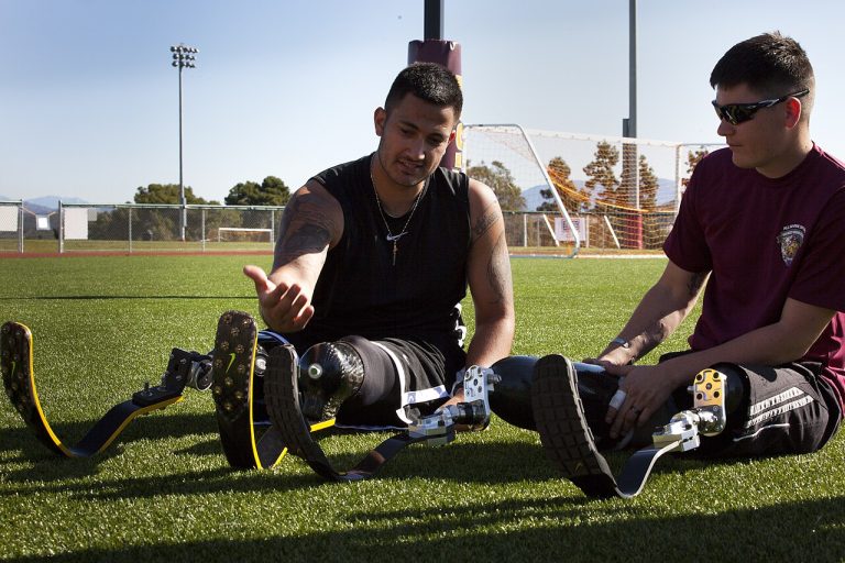 Two athletes with advanced running-blade prosthetic legs sitting together on a sports field