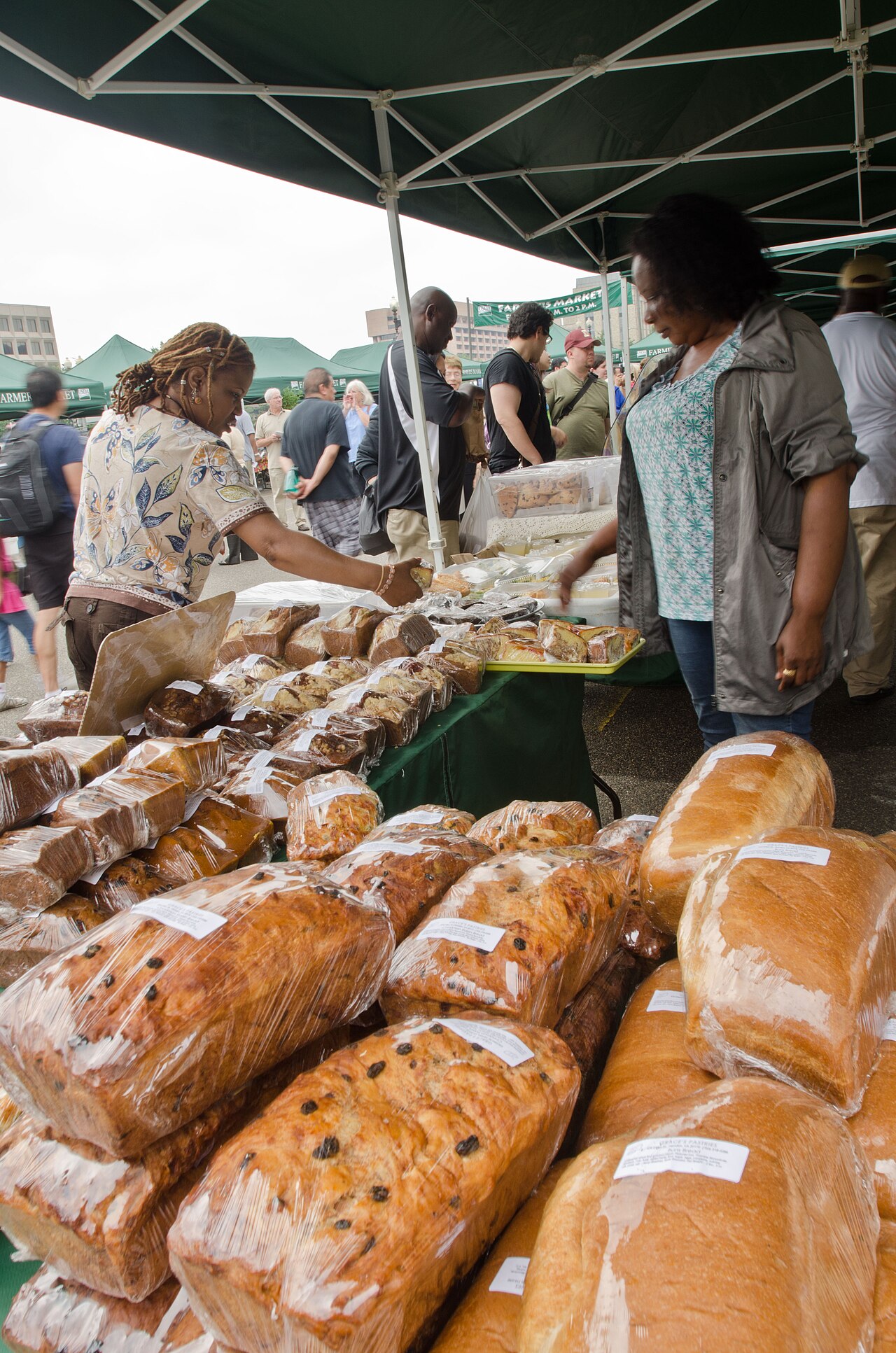 A baked goods vendor selling bread directly to a customer at a farmers market stand