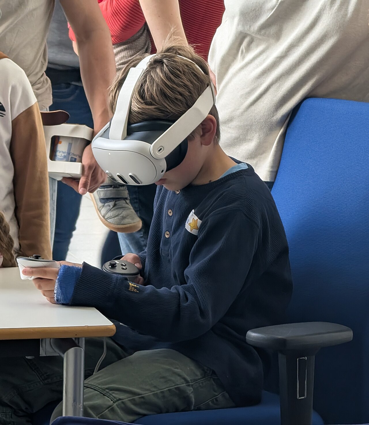 A boy wearing a Meta Quest VR headset and holding controllers while seated at a table