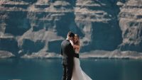 A bride and groom embracing on a cliff overlooking a lake and mountain cliffs
