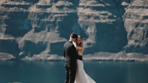 A bride and groom embracing on a cliff overlooking a lake and mountain cliffs