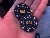 A hand holding two black casino chips marked with the value 100
