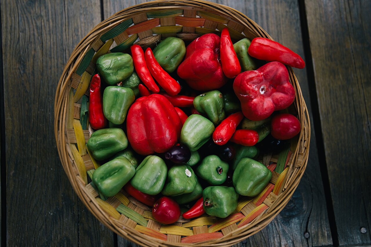 A woven basket filled with colorful peppers and fresh vegetables
