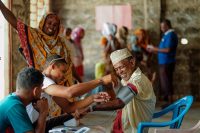 A community health worker checking blood pressure with people smiling nearby