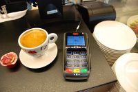 A contactless payment terminal on a cafe counter next to a cup of coffee