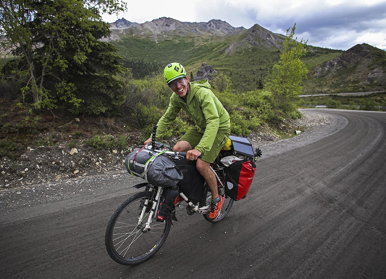 A cheerful cyclist riding a loaded touring bike on a mountain road