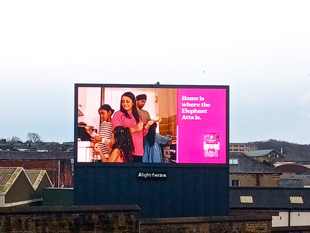 A large digital LED billboard displaying an advertisement above city rooftops