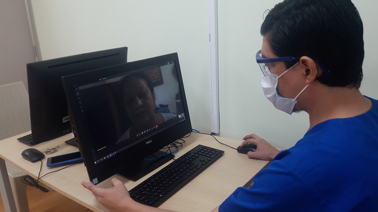 A doctor wearing a mask attending a patient by video teleconsultation