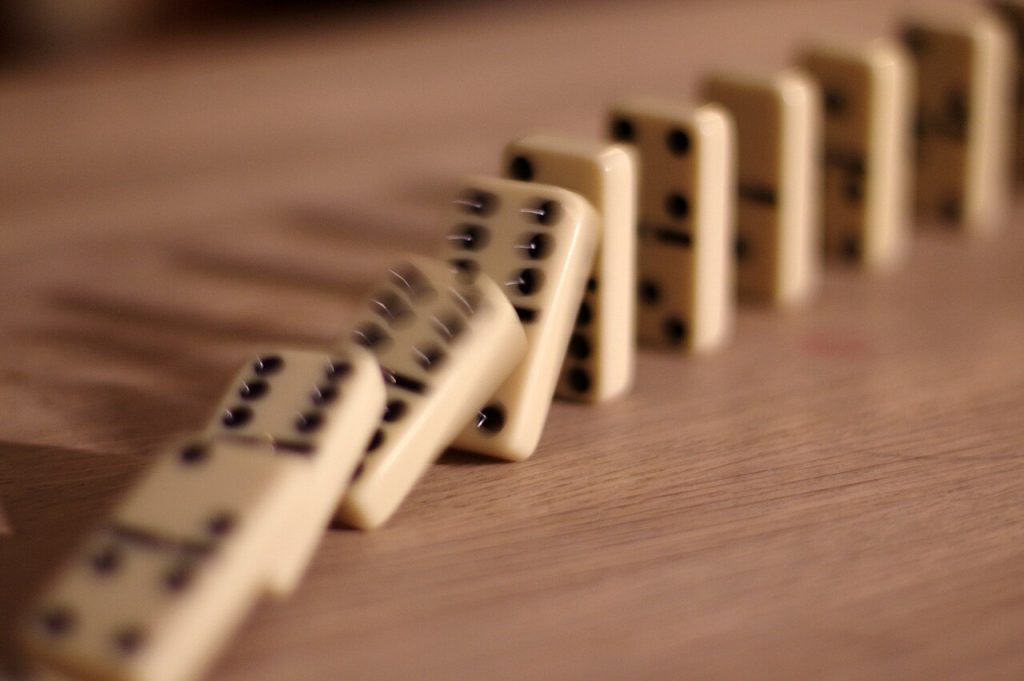 A row of dominoes captured mid-fall, each one toppling the next
