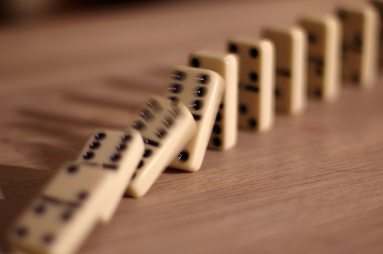 A row of dominoes captured mid-fall, each one toppling the next