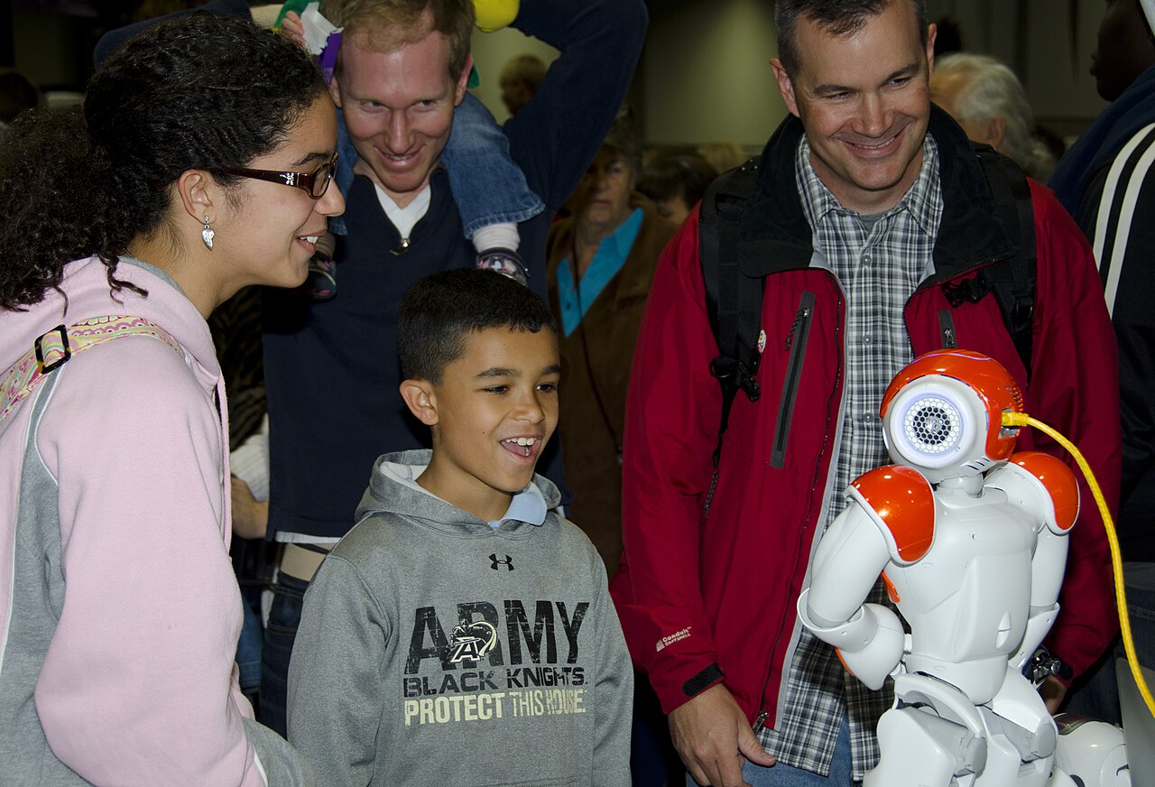 A family smiling and interacting with a small humanoid robot at a science festival