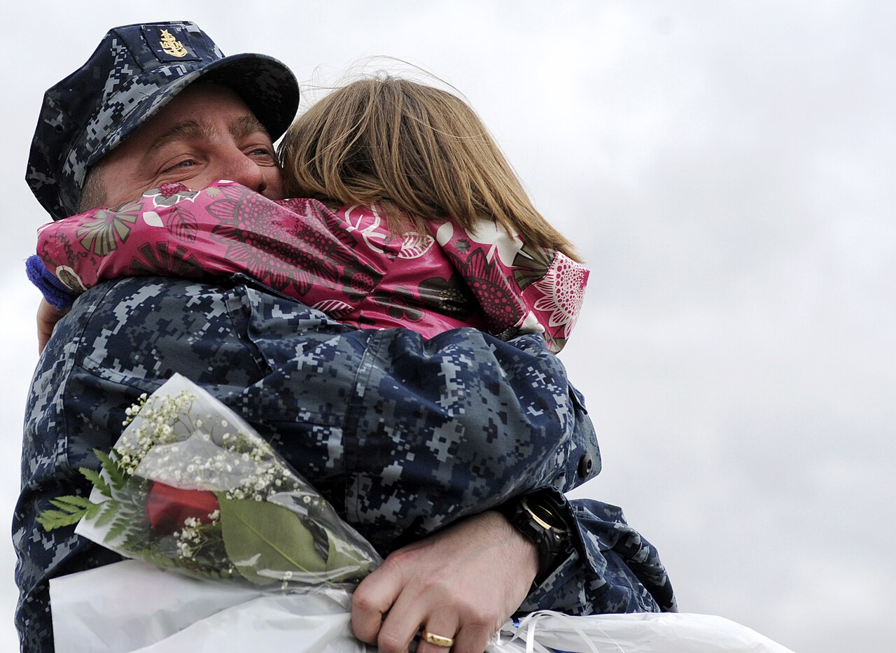 A father in military uniform embracing his young daughter during an emotional homecoming reunion