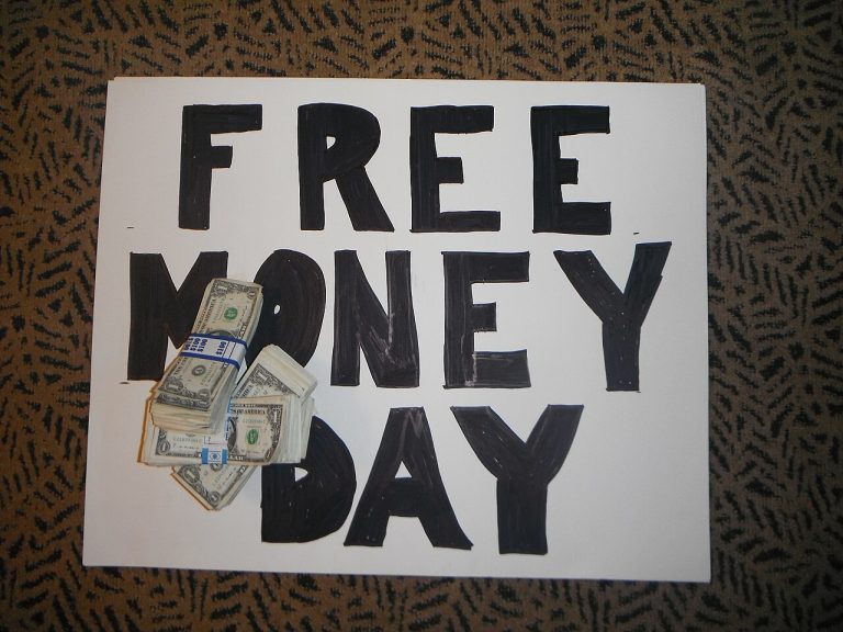 A hand-lettered Free Money Day sign with a stack of real cash placed on top
