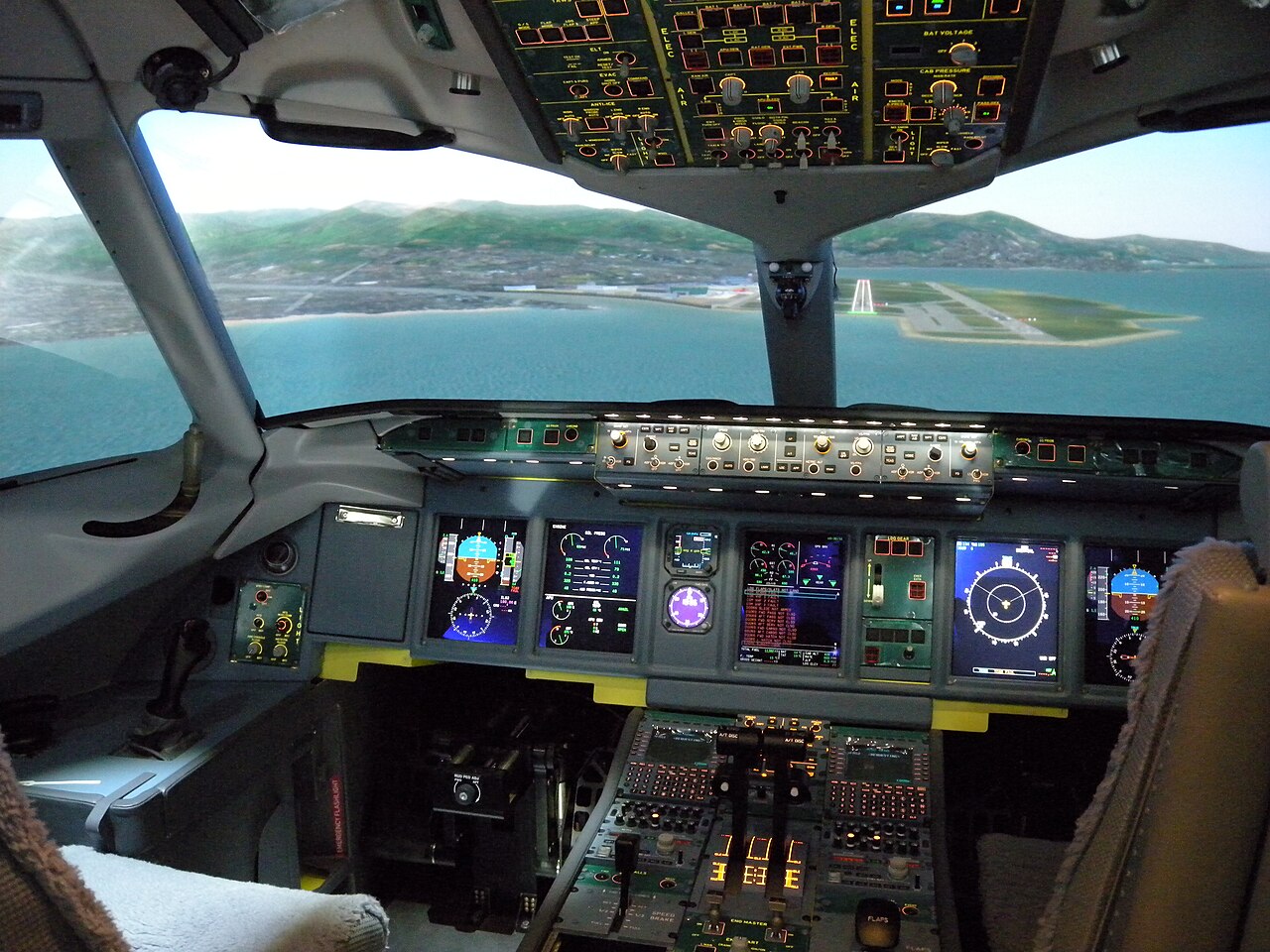 The cockpit interior of a full-motion airline flight simulator showing a projected runway approach