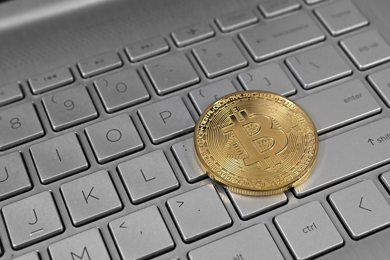 A gold Bitcoin coin resting on a laptop keyboard