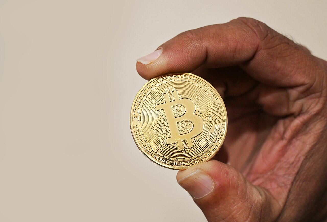 A hand holding a gold Bitcoin cryptocurrency coin