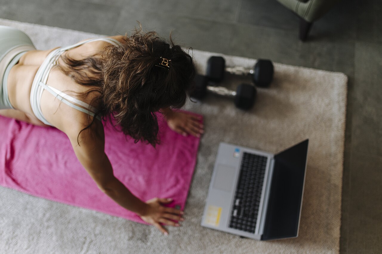 A woman doing a home workout on a yoga mat next to a laptop and dumbbells
