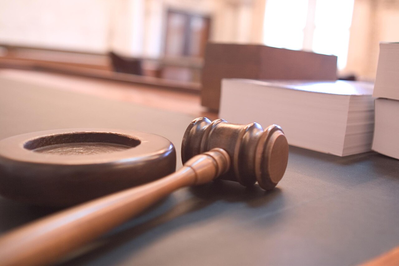 A wooden judge's gavel resting on a courtroom table beside stacks of legal documents