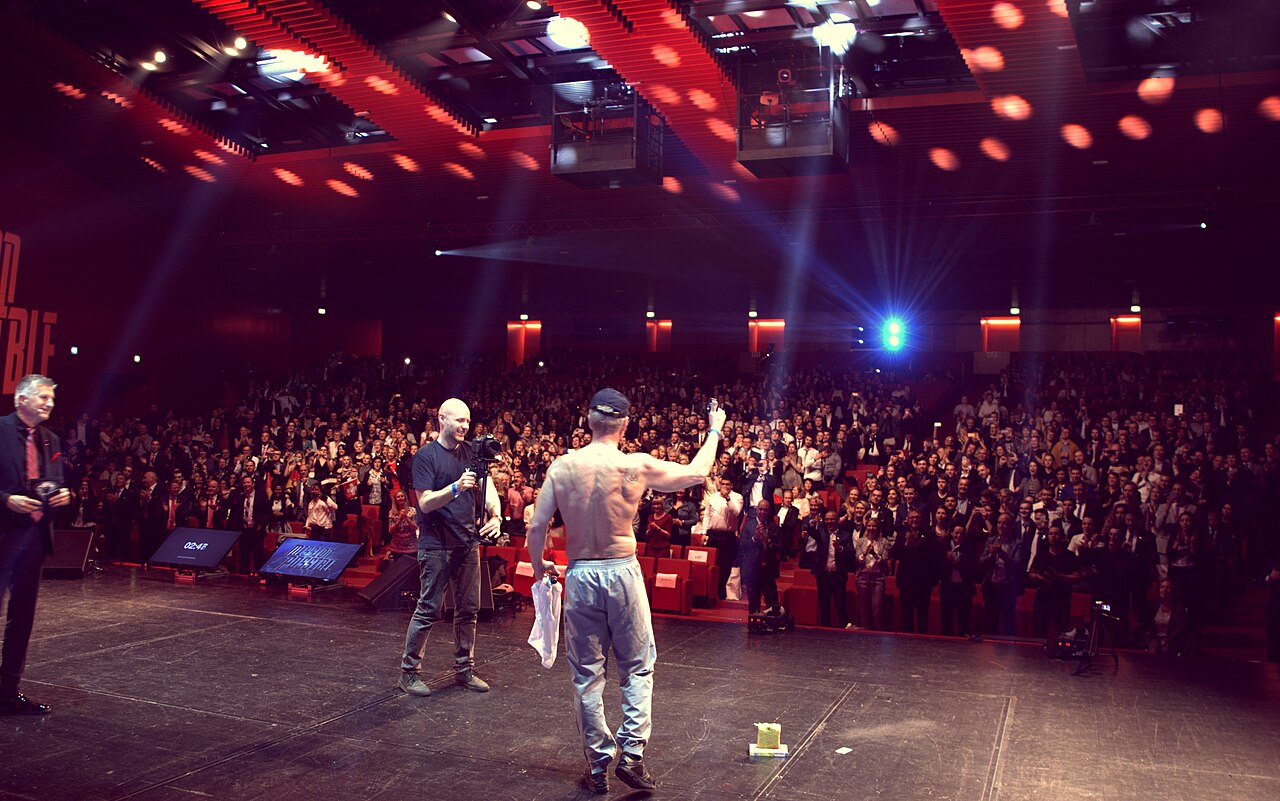 A large audience of people gathered at a network marketing company convention with stage lighting