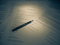 A legal contract document with a pen resting on a section about payments and compensation