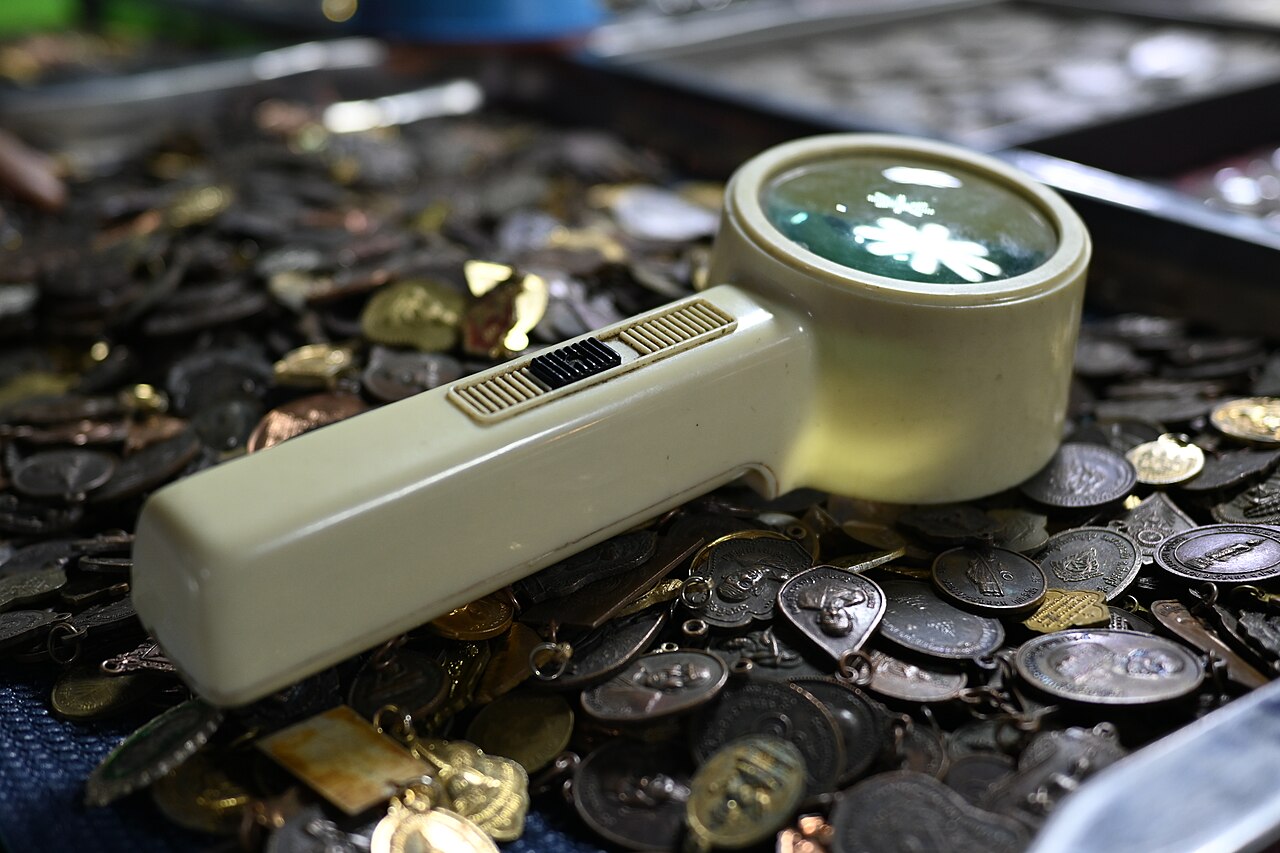 A handheld magnifying glass resting on a scattered pile of coins and medallions