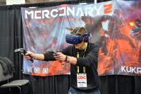A young man wearing a VR headset and holding controllers while playing a game at a convention booth