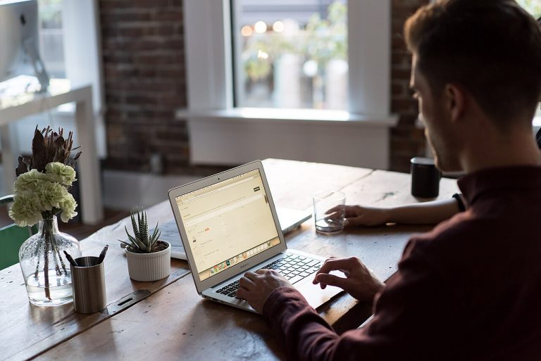 A man working on a laptop at a wooden desk in a bright home office