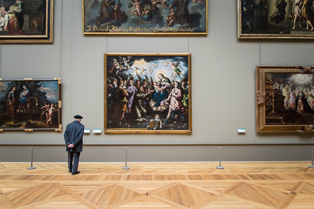 A museum visitor standing alone viewing an original framed painting on a gallery wall