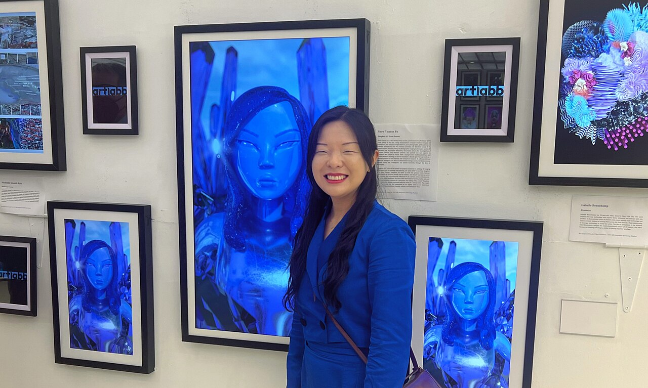 A woman posing in front of framed digital NFT artwork displayed on screens at a gallery exhibition