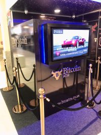 A physical Bitcoin ATM kiosk with a screen advertising buying a car with Bitcoin