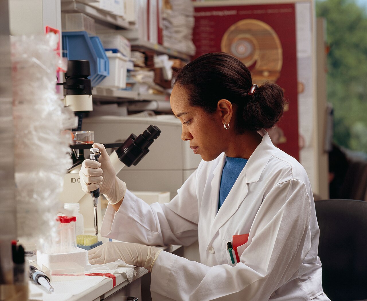 A researcher in a lab coat examining a sample through a microscope while holding a pipette