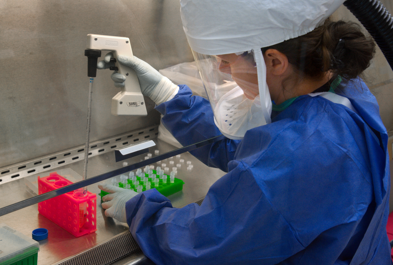 A scientist in full protective gear handling laboratory vials inside a biosafety cabinet