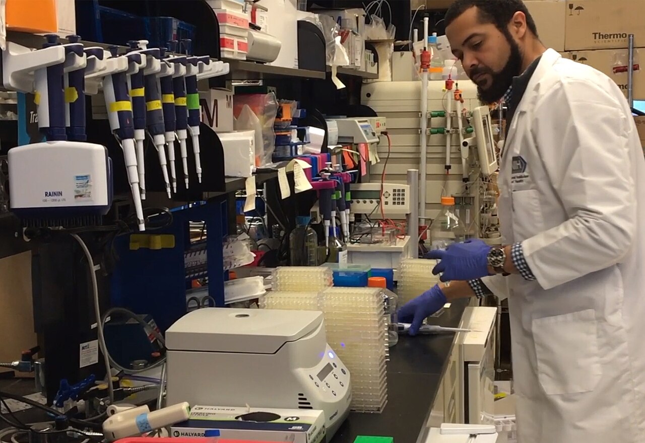 A scientist in a lab coat working with pipettes and lab equipment researching a COVID-19 vaccine