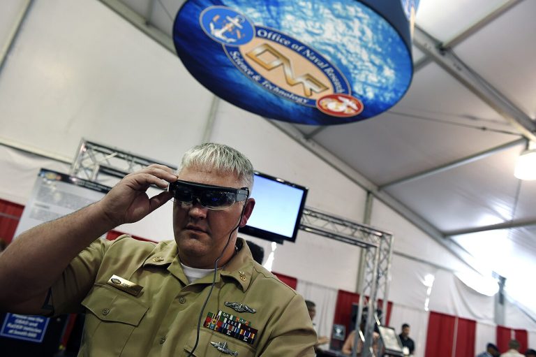 A service member demonstrating a pair of augmented reality glasses at a technology showcase