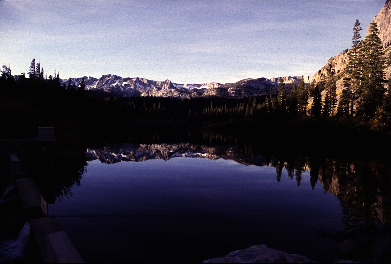 A perfectly still mountain lake reflecting the surrounding peaks and forest like a mirror