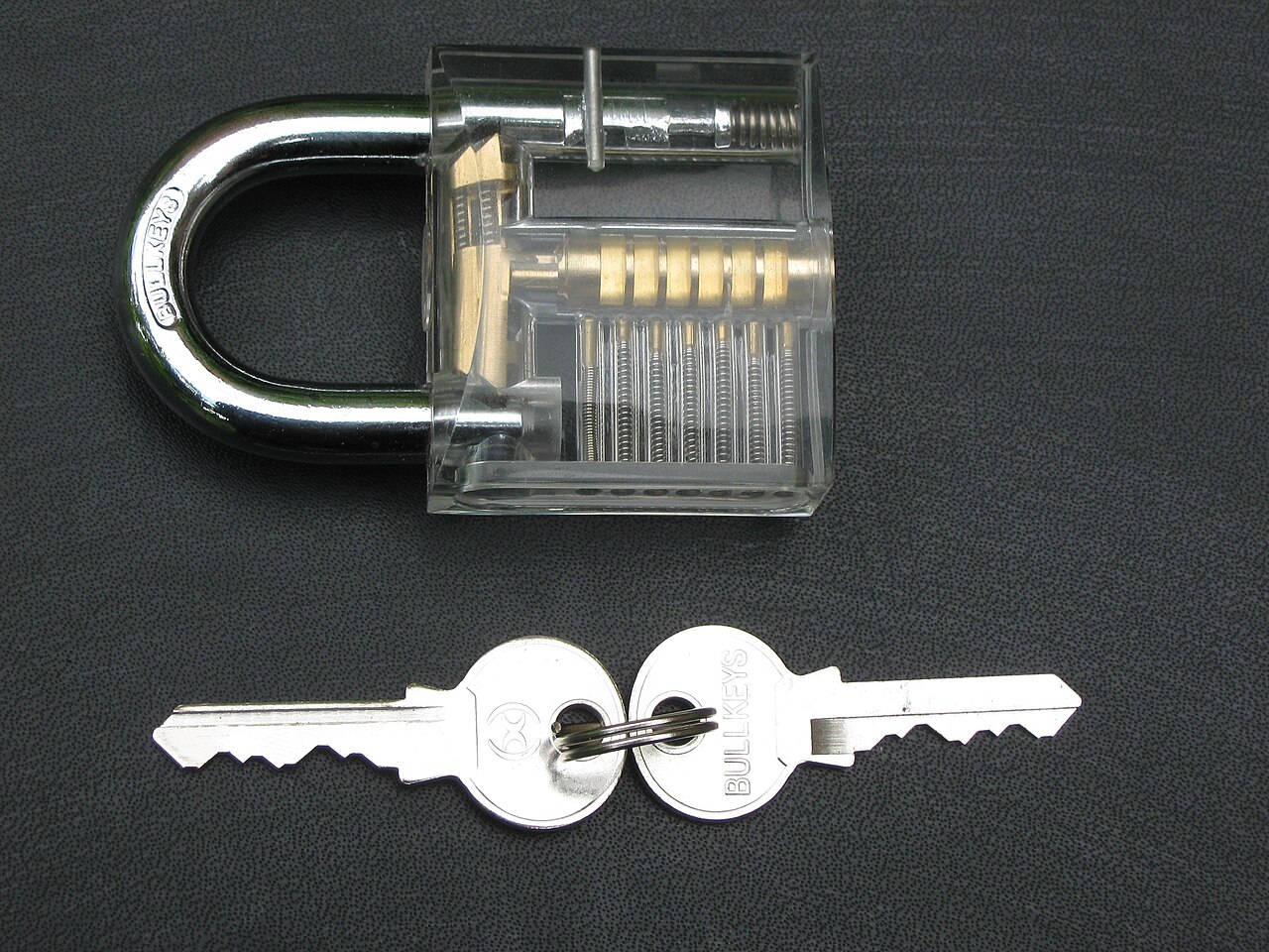 A transparent padlock showing its internal mechanism next to a pair of matching keys