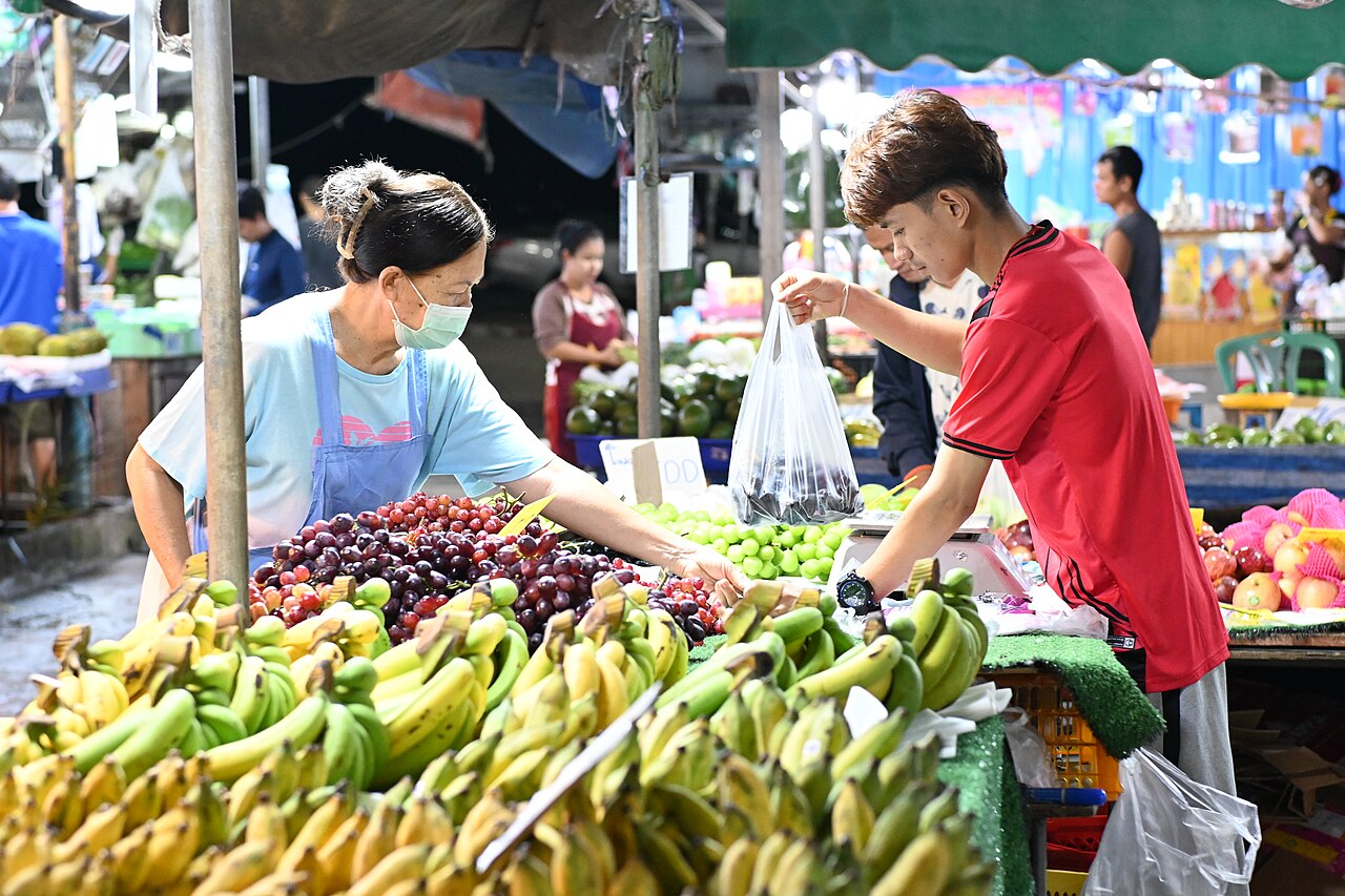 A vendor handing a bag of fresh fruit directly to a customer at an outdoor market stall