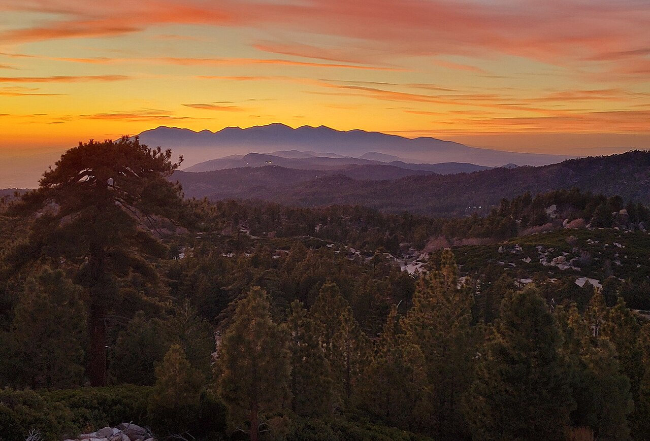 A vivid orange and pink sunset silhouetting mountain ranges and forest