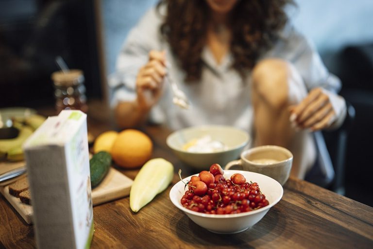 A woman enjoying a healthy breakfast with fresh fruit, yogurt, and coffee at home