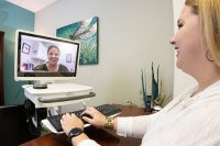A woman smiling during a video call consultation on a computer monitor