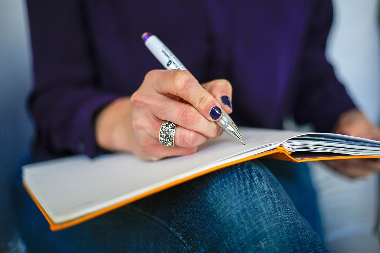 A close-up of a woman writing in a journal with a pen